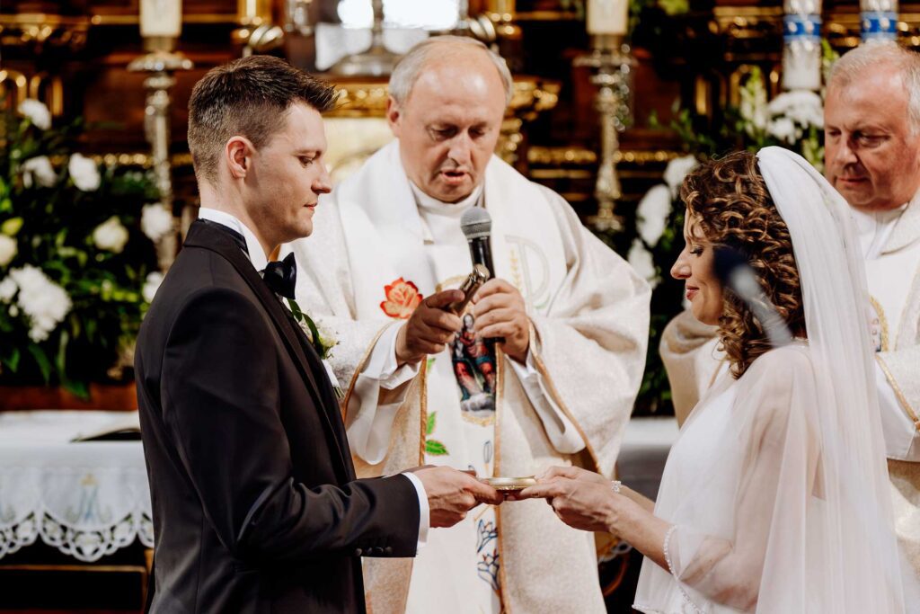Ksiądz kropi wodą święconą obrączki ślubne trzymane przez młodych.