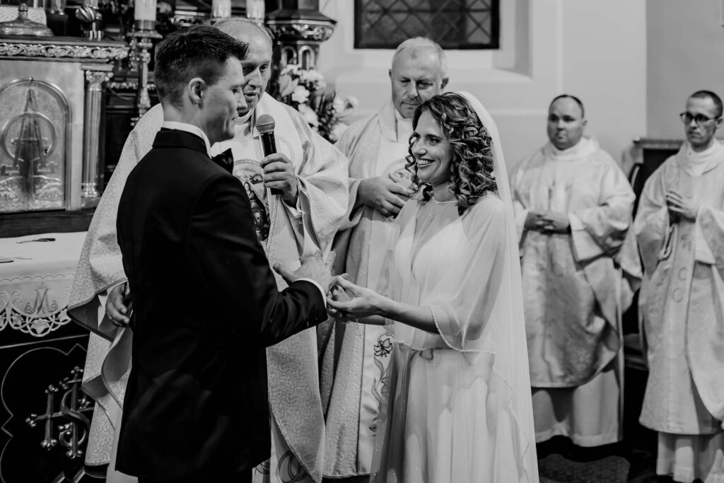 Czarno-białe zdjęcie Pary Młodej w trakcie ceremonii zaślubin w kościele.