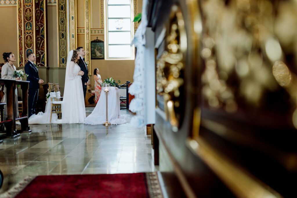 Widok na Parę Młodą stojącą przy ołtarzu z perspektywy nawy kościoła.