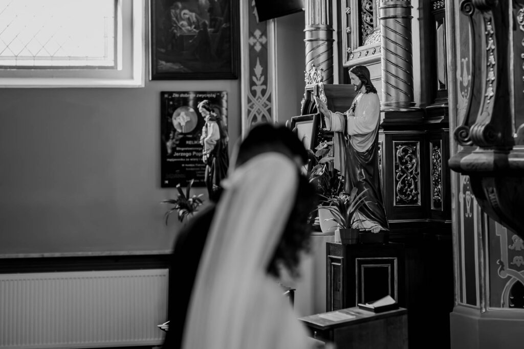 Czarno-biały detal kościoła z figurą sakralną i sylwetką nowożeńców.
